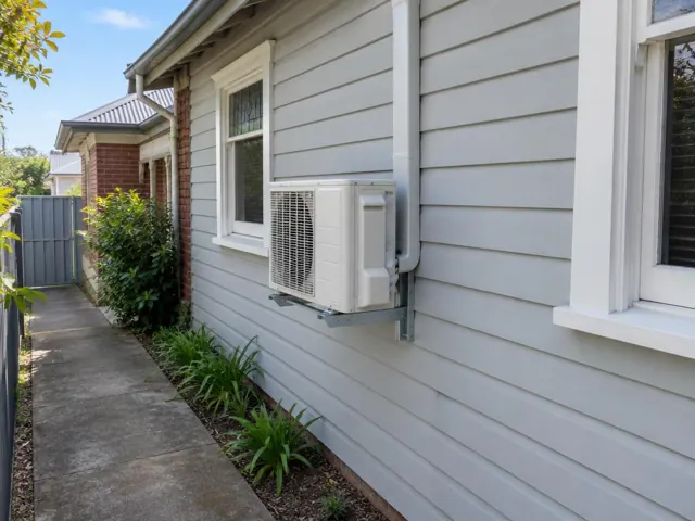 Wall-mounted outdoor air conditioner on a weatherboard house beside a side path in Salisbury