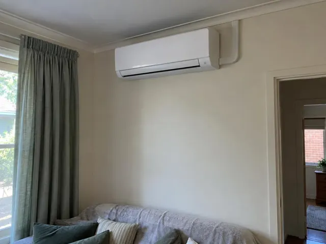 Wall-mounted split system above a sofa in a beige living room with curtains in Salisbury